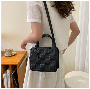 Detail of black waffle-textured square handbag with top handle and adjustable strap