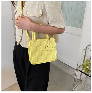 Detail of yellow biscuit-shaped crossbody bag with quilted texture and cheese charm