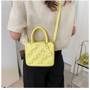Macro detail of yellow biscuit textured crossbody bag with cheese pendant accessory