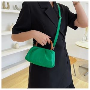 Detail of green ruched cloud bag with wooden ring handle and adjustable strap on a model