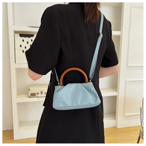 Detail of light blue pleated cloud bag with brown wooden handle and gold hardware detail
