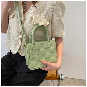Detail of light green cookie bag featuring cubic texture and cheese pendant accessory