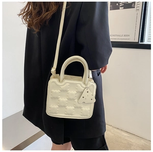 Detail of cream white quilted mini bag featuring a unique cheese pendant and thin strap