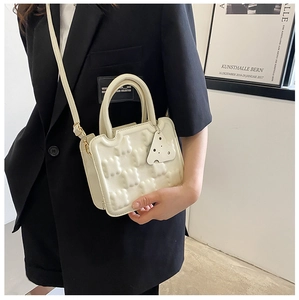 Detail view of cream structured crossbody bag with cheese charm and metal buckle accents