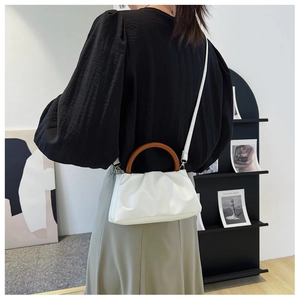 Detail of white cloud pleated crossbody bag with natural wood handle and PU leather