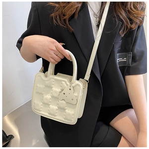 Detail of cream white waffle-textured mini handbag featuring a unique cheese pendant