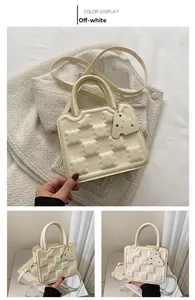 Detail of creamy white biscuit textured handbag with cheese pendant and shoulder strap