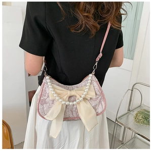 Pink lace crossbody bag with oversized silk bow and pearl chain worn by a model