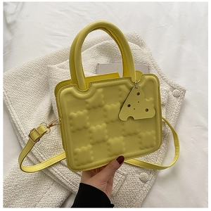 Detail of yellow waffle-shaped crossbody bag with a cute cheese pendant and adjustable strap