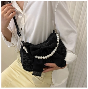Detail of black bow bag with white pearl chain worn over a white shirt and yellow skirt