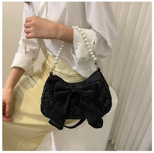 Detail of a black pleated handbag featuring a large satin bow and pearl bead handle