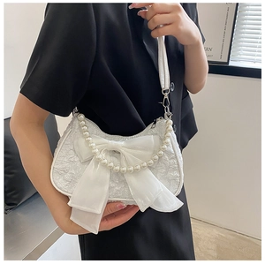 Close-up of white pleated shoulder bag featuring chiffon bow and pearl chain details