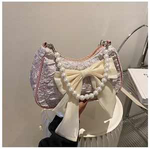 Detail of lavender pleated underarm bag featuring a cream bow and pearl handle