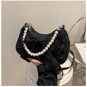 Detail of a vintage black bow bag with textured fabric and elegant pearl handle strap