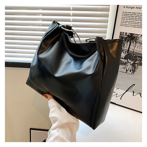Detail of soft black leather tote bag featuring a minimalist silver metal ring handle