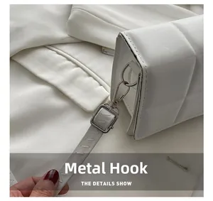 Detail of silver hardware hook and plaid embossed texture on a white crossbody bag