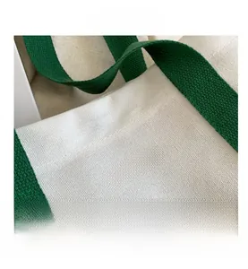 Detail view of white canvas tote bag with green handles and black FASHION lettering