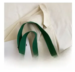 Detail of reinforced green fabric handles on a cream canvas tote bag for daily use