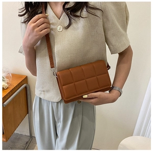 Detailed view of brown quilted crossbody bag with padded square pattern and slim strap