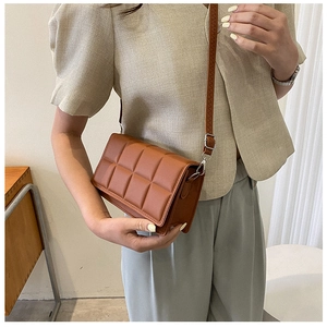 Close-up of a brown quilted crossbody bag with block texture on a female model