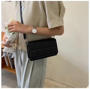 Detail of a black quilted leather crossbody bag with silver buckles on a thin strap
