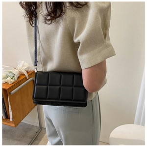 Detailed view of black quilted flap bag with thin shoulder strap on a female model