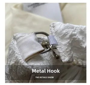 Detail showing the silver metal hook and pearl handle on a white pleated cloud bag