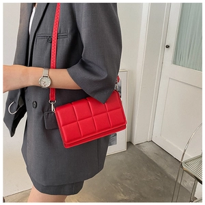 Close-up of a red quilted crossbody bag with a padded checkerboard pattern and shoulder strap