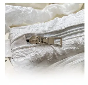Detail of smooth metal zipper and textured pleated fabric on a white pearl chain bag