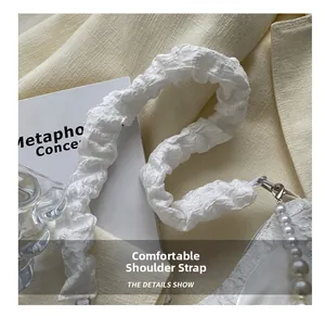Detail of white pleated shoulder strap with pearl charms and metal lobster clasp