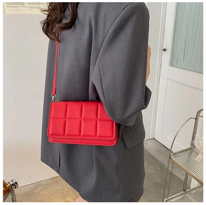Detail of red quilted crossbody bag with textured square pattern worn with grey blazer