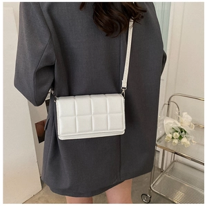 Detailed back view of a quilted white leather crossbody bag worn with a grey blazer