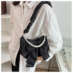 Close-up of black pleated cloud bag with a large satin bow and pearl chain strap