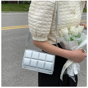Detail shot of a silver quilted crossbody bag featuring puffy leather squares and metallic finish