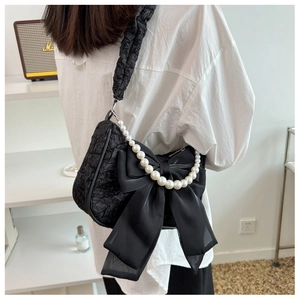 Detail of black pleated cloud bag featuring oversized satin bow and pearl chain handle