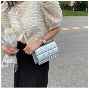 Silver quilted square crossbody bag with metallic finish shown in a stylish outdoor setting