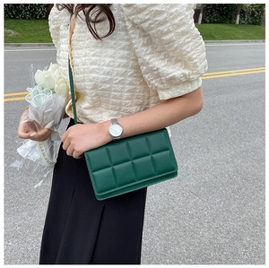 Close-up of a dark green quilted crossbody bag with a classic checkered pattern texture