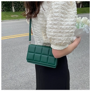 Detail of dark green quilted crossbody bag with plaid texture and slim shoulder strap
