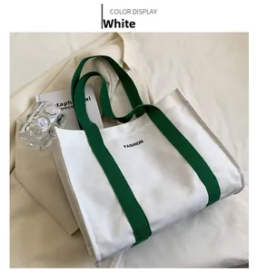 Detail of minimalist white canvas tote with green straps and black FASHION lettering