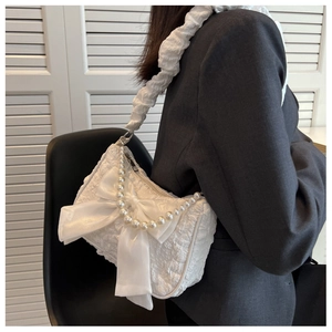 Detail of white pleated shoulder bag featuring pearl chain and large bow accent