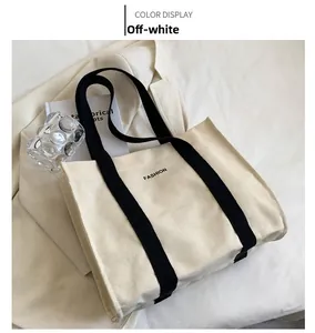 Detail of off-white canvas tote bag with black contrast handles and fashion slogan