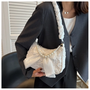 Detail of white pleated cloud bag featuring large silk bow and elegant pearl chain