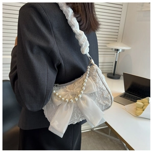 Detail of white pleated underarm bag featuring large satin bow and pearl chain decoration