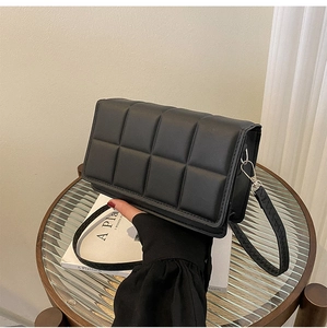 Detail of black quilted square crossbody bag with textured puff padding and silver metal buckle