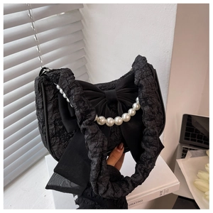 Detail of black pleated shoulder bag with oversized satin bow and white pearl chain