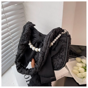 Detail of black pleated cloud bag featuring a large bow and elegant pearl chain handle