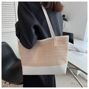 Straw tote bag with white leather trim shown on shoulder in a minimalist indoor office setting