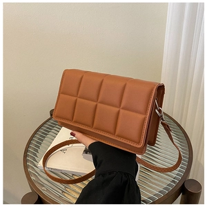 Detailed view of brown quilted crossbody bag with textured faux leather on a glass table