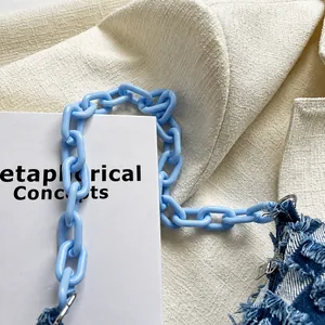 Macro-detail van een lichtblauwe schakelketting op een donkerblauwe denim schoudertas