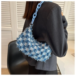 Detail van blauw-wit geruite denim baguette tas met franjes en een dikke kunststof ketting